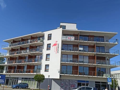 biały budynek z balkonami i samochody zaparkowane przed nim w obiekcie Flamingo Apartments w mieście Międzyzdroje