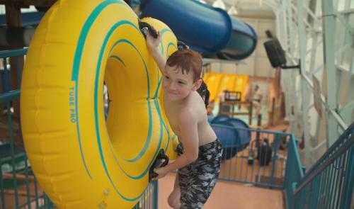 a young boy is standing next to a yellow tube at Americana Waterpark Resort & Spa in Niagara Falls