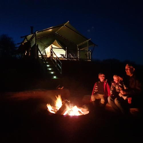 a group of people sitting around a camp fire at Brackenhill Glamping - Safari Tent with Hot Tub in Ivybridge