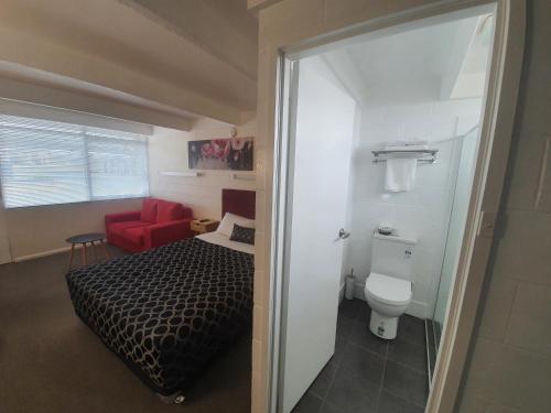 a small bedroom with a bed and a red chair at Charles Sturt Motor Inn in West Wyalong