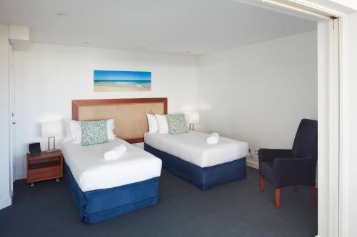 a hotel room with two beds and a chair at Seashells Mandurah in Mandurah