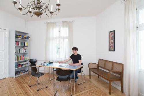 un hombre sentado en una mesa en una habitación en Jugendgästehaus des CVJM Berlin-Kaulsdorf, en Berlín