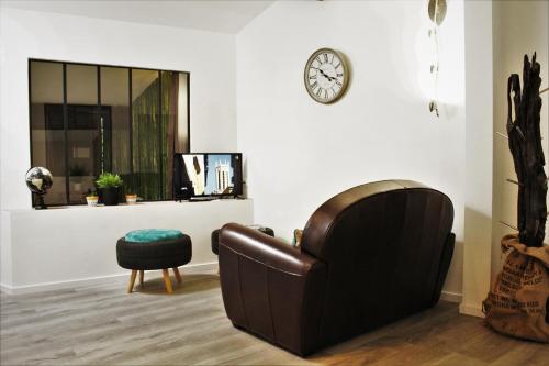 a living room with a leather chair and a clock on the wall at Gîte Esprit Loft Proche de Narbonne in Mirepeisset
