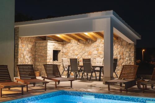 eine Terrasse mit Stühlen und ein Pool in der Nacht in der Unterkunft Villa Green Oasis in Lovreć