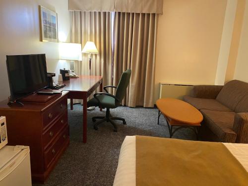 a hotel room with a couch and a desk with a television at Northern Star Hotel & Convention Center in Slave Lake