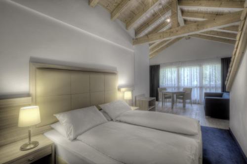 a bedroom with a white bed and a living room at Hotel La Tambra in Corvara in Badia