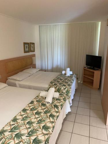 a hotel room with two beds and a television at Beach Class Slin Muro Alto in Porto De Galinhas