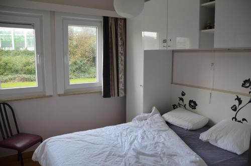 a bedroom with a white bed and two windows at De Haan - Dahlia 007 in De Haan