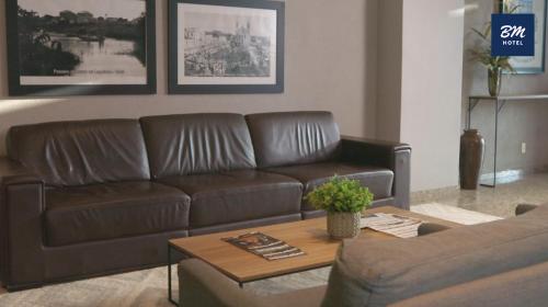 a brown leather couch in a living room with a table at BM Hotel in São Sebastião do Paraíso