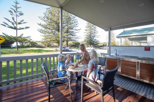 a woman and two children sitting at a table on a deck at Werri Beach Holiday Park in Gerringong