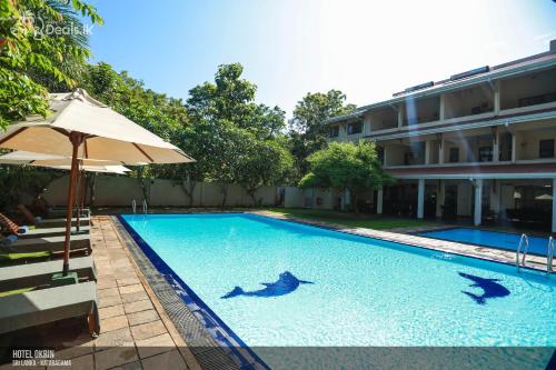 zwei Delfine schwimmen in einem Pool mit Sonnenschirm in der Unterkunft Lavendish Okrin Hotel in Kataragama