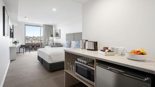 a hotel room with a bed and a kitchen with fruit on a counter at Oaks Toowoomba Hotel in Toowoomba