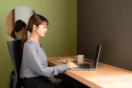 a woman sitting at a desk with a laptop computer at The OneFive Kyoto Shijo in Kyoto