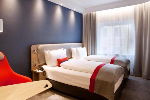 a hotel room with two beds and a red chair at Holiday Inn Express Frankfurt Airport - Raunheim, an IHG Hotel in Raunheim