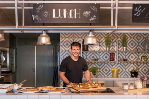 a man standing behind a counter in a kitchen with food at Stayokay Hostel Maastricht in Maastricht