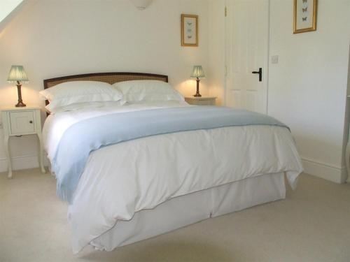 1 dormitorio con 1 cama grande con sábanas y almohadas blancas en Well Cottage B and B, en Cirencester