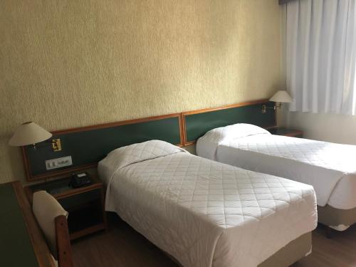 a hotel room with two beds with white sheets at Duomo Park Hotel in Curitiba