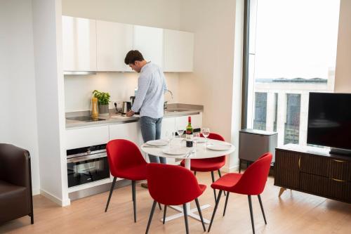 a man in a kitchen with a table and red chairs at PREMIER SUITES PLUS Amsterdam in Amsterdam