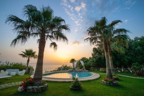 a pool with palm trees and the ocean at sunset at CapoSperone Resort in Palmi