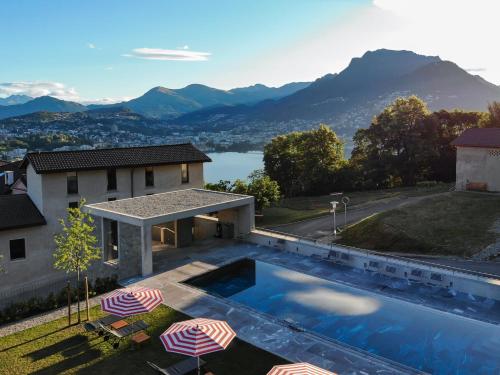 a swimming pool with umbrellas and a house with mountains at Bigatt Hotel & Restaurant in Lugano