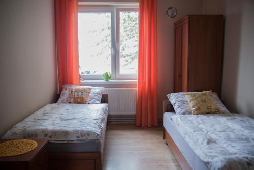 a bedroom with two beds and a window with orange curtains at Pod Kogucikiem in Krzyżanowice
