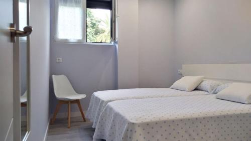 a white bedroom with two beds and a chair at Apartamento los Acantilados Nº 2 Cobreces in Cóbreces