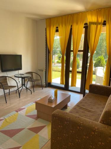 a living room with yellow curtains and a couch and a table at Apartment Aquareumal Fojnica in Fojnica