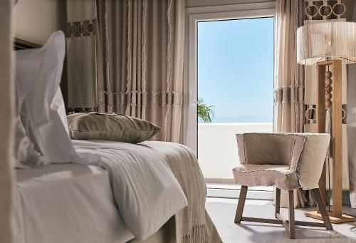 a bedroom with a bed and a chair and a window at Palladium Hotel in Platis Yialos Mykonos
