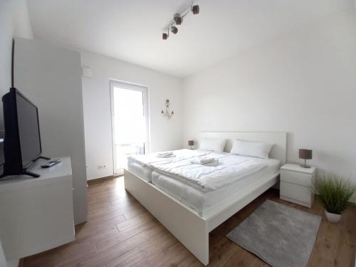 a white bedroom with a white bed and a tv at Ferienhaus Piel - Am Inselwald in Ueckeritz