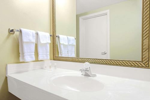 La salle de bains est pourvue d'un lavabo blanc et d'un miroir. dans l'établissement Days Inn by Wyndham St. Louis/Westport MO, à Maryland Heights