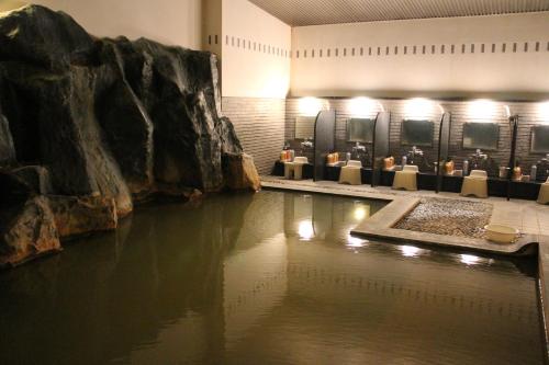 a pool of water in a room with a large rock at Biei Shirogane Onsen AONOBI YUYU in Biei