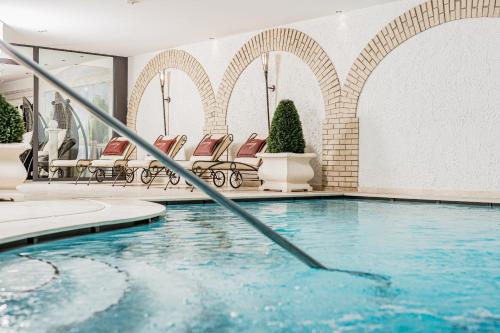 ein Pool in einem Hotel mit Stühlen im Hintergrund in der Unterkunft Savoy Dolomites Luxury & Spa Hotel in Wolkenstein in Gröden