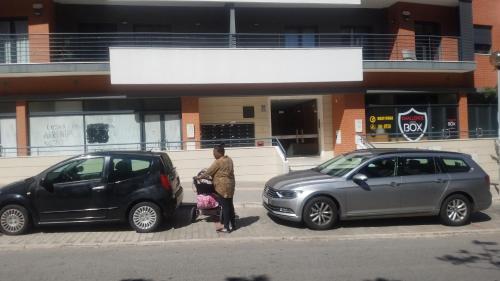 una mujer parada entre dos coches delante de un edificio en ADALBERTO NASCIMENTO LUXURY APARTA-HOSTEL At COLINAS DO CRUZEIRO en Odivelas