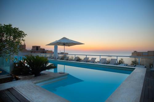 a swimming pool with an umbrella and chairs and the ocean at The George, Urban Boutique Hotel in St Julian's