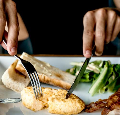 a person holding a fork and knife over a plate of food at Sand in My Shoes Beach Loft in Thong Nai Pan Noi