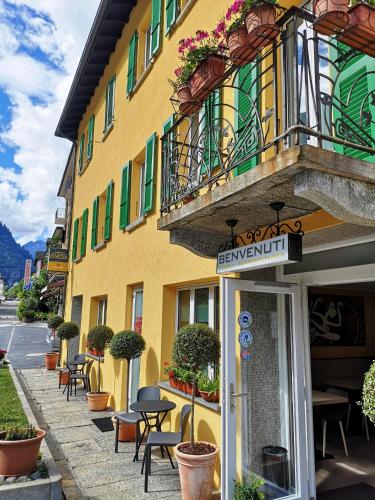 un bâtiment jaune avec des tables et des chaises devant lui dans l'établissement Hotel Elvezia, à Lavorgo