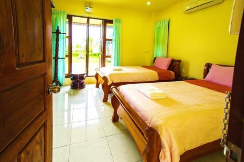 two beds in a room with yellow walls at Suan Luang Garden View in Nong Khai