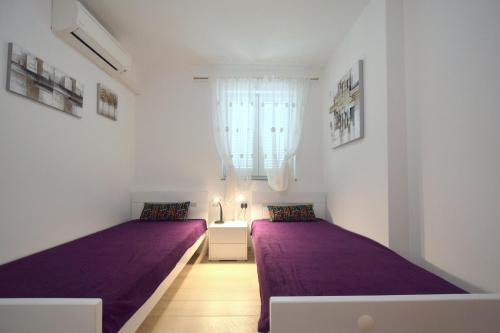 two beds in a room with purple sheets and a window at Apartment Acija in Malinska