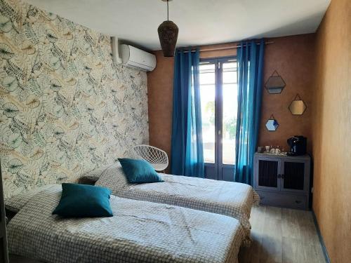 a bedroom with two beds and a window with blue curtains at Villa Lei Rigaü in Salernes