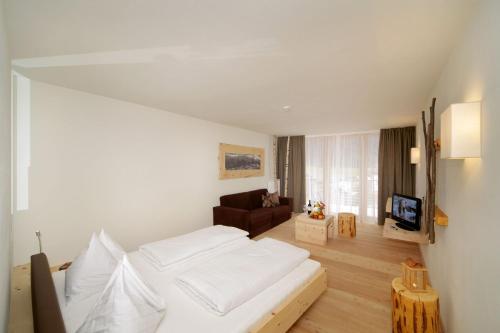 a bedroom with a white bed and a living room at Vitalhotel Rainer in Ultimo