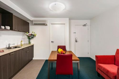 a kitchen and dining room with a table and a red chair at Melbourne Carlton Central Apartment Hotel Official in Melbourne
