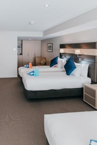 a hotel room with three beds with blue pillows at Novotel Newcastle Beach in Newcastle