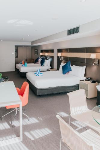 a hotel room with two beds and tables and chairs at Novotel Newcastle Beach in Newcastle