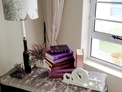 a pile of books on a table with a clock and a lamp at Gordon's Beach Lodge in Gordonʼs Bay