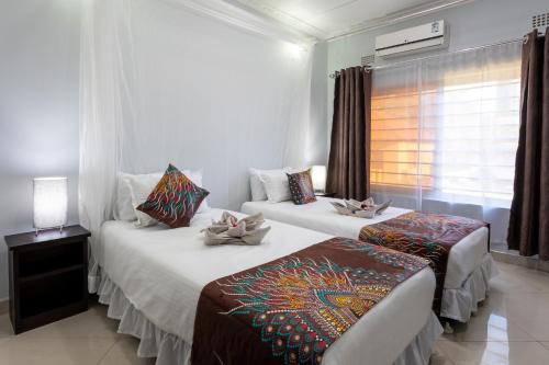 two beds in a hotel room with a window at Nzubo Experience in Livingstone