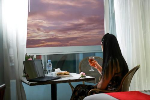 Mermaid Beach Hotel LLC في عجمان: امرأة تجلس على طاولة مع كوب من النبيذ