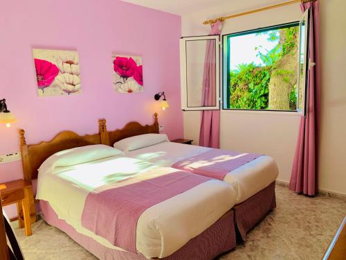 a bedroom with a bed with pink walls and a window at Villa CAROLINA in Cala en Forcat