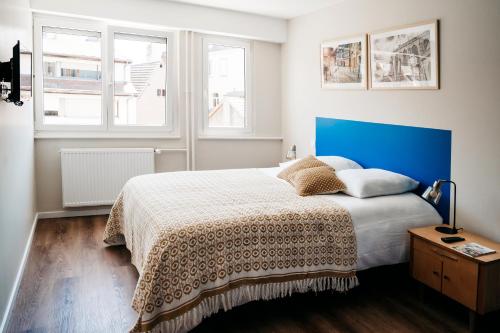 a bedroom with a bed with a blue headboard and two windows at LE 19 KLEBER climatisé in Colmar