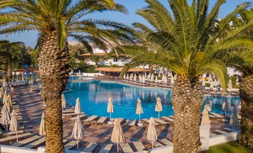 a pool with palm trees and chairs and umbrellas at Lagas Aegean Village in Kardamaina