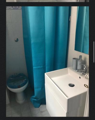 a bathroom with a toilet and a blue shower curtain at the goat on the beach in Scilla